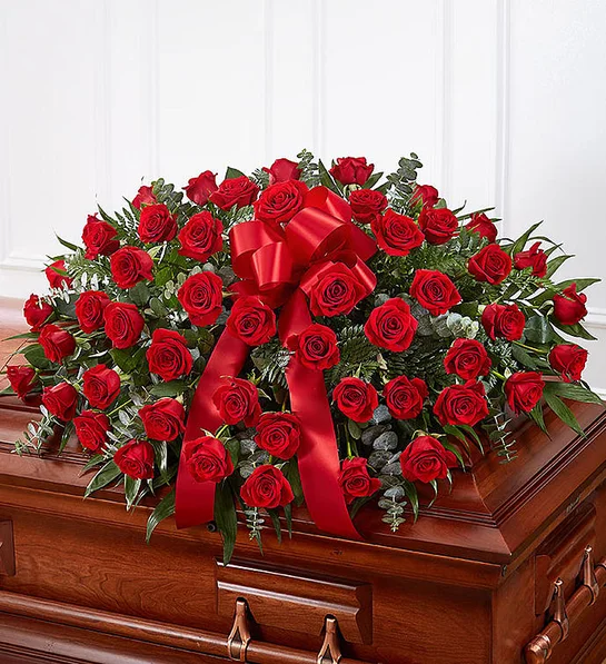 Half casket crafted with over 50 premium red roses, fresh greenery, and accented with a red satin ribbon